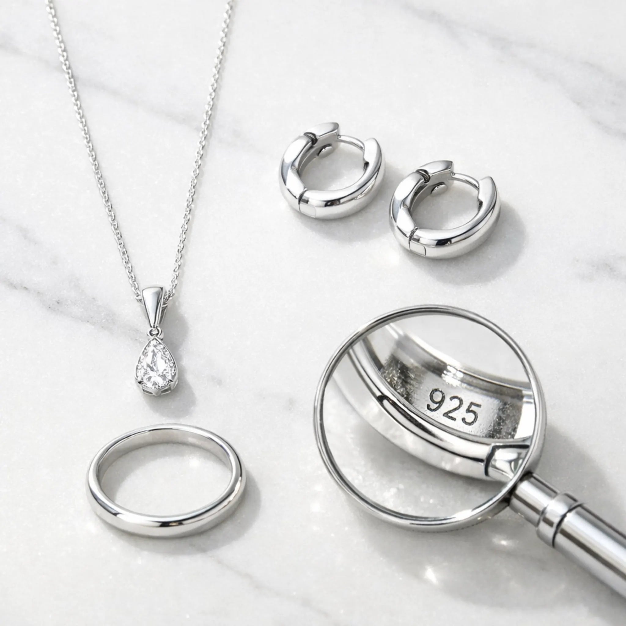 Sterling silver jewelry pieces including 925 hallmarked necklace, hoop earrings and ring on white marble surface - affordable hypoallergenic jewelry