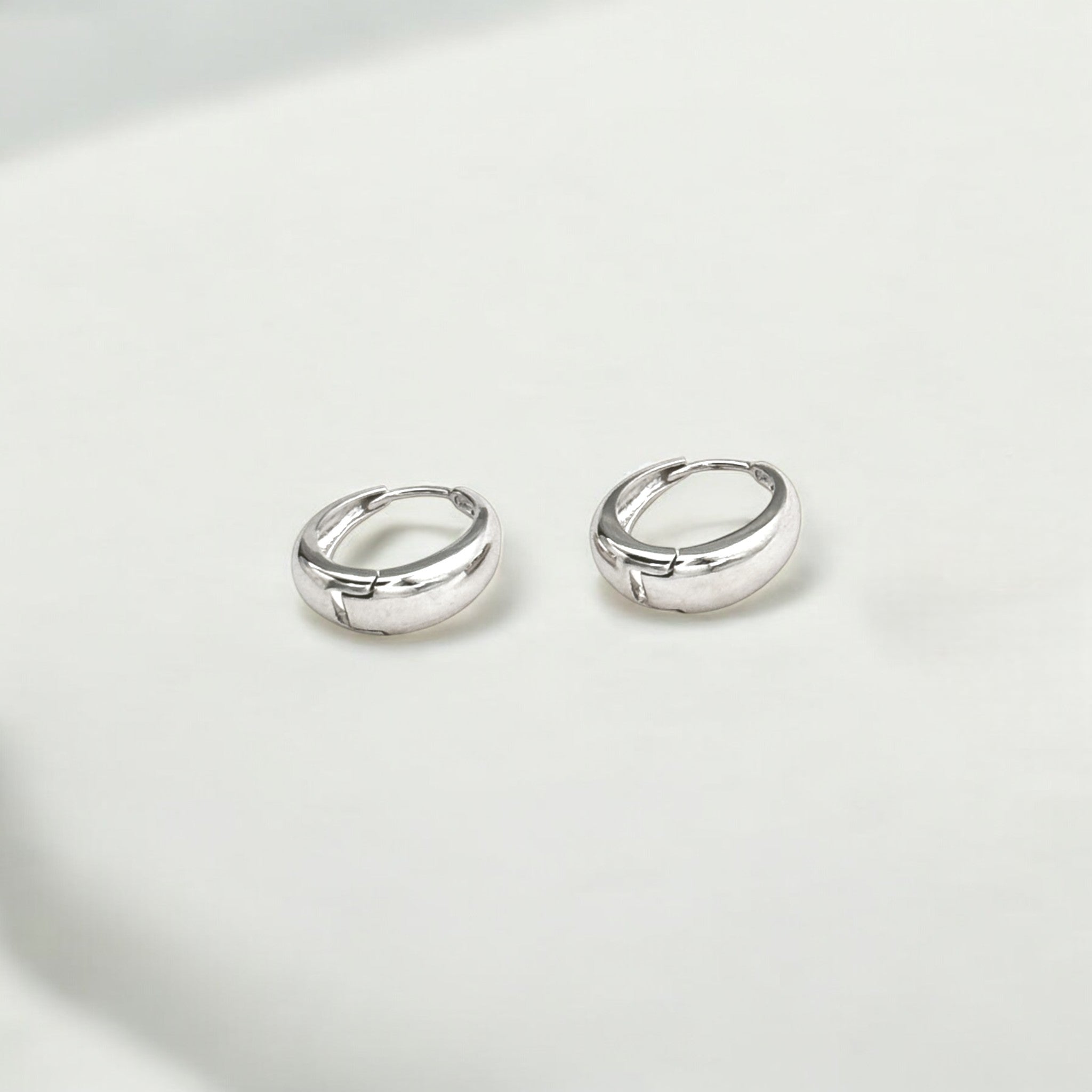 Close-up of Hermin's Eclipse Silver Dome Huggie Hoops in sterling silver with rhodium finish, crafted for elegance and durability