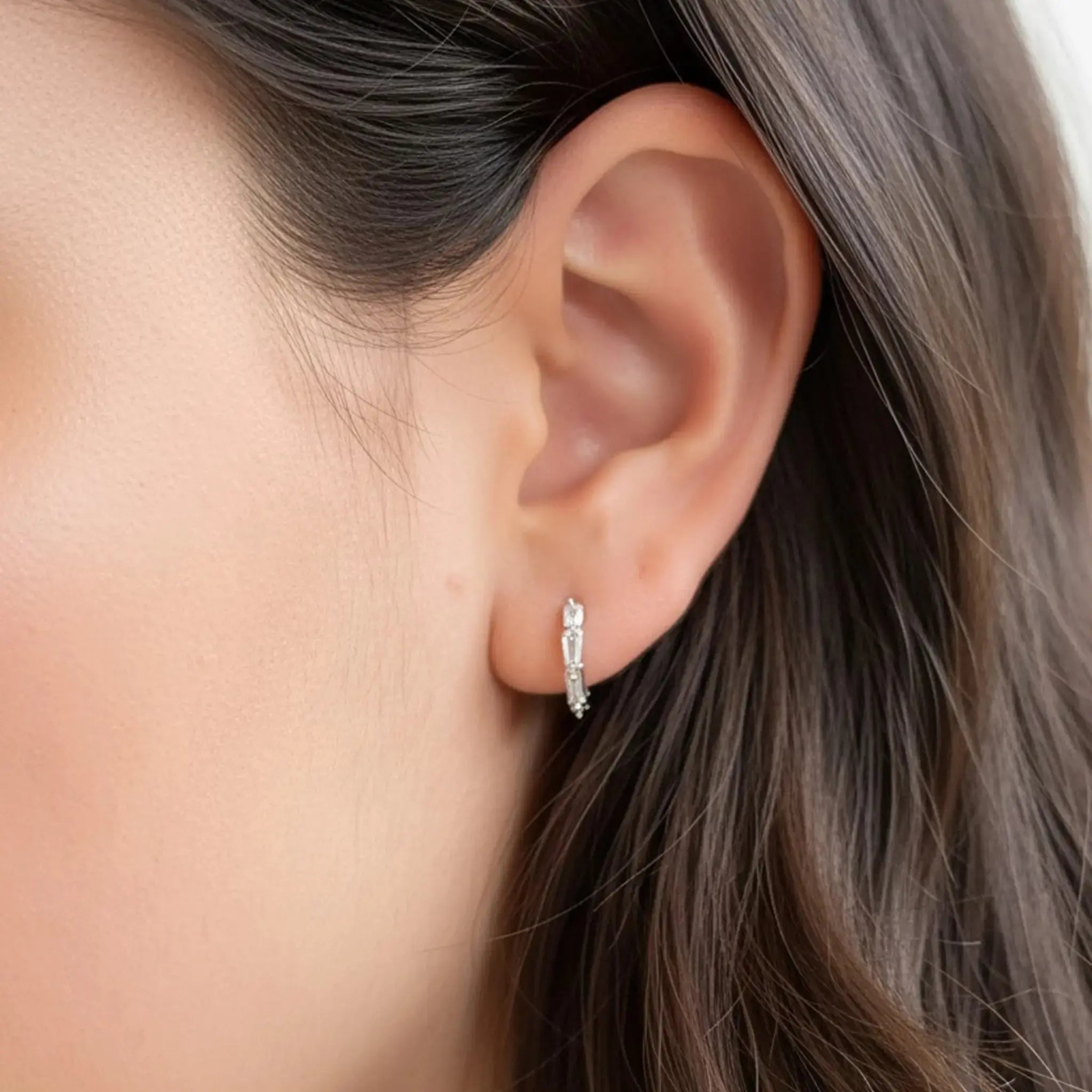 Model wearing hypoallergenic sterling silver tapered baguette huggie hoop earrings with rhodium vermeil
