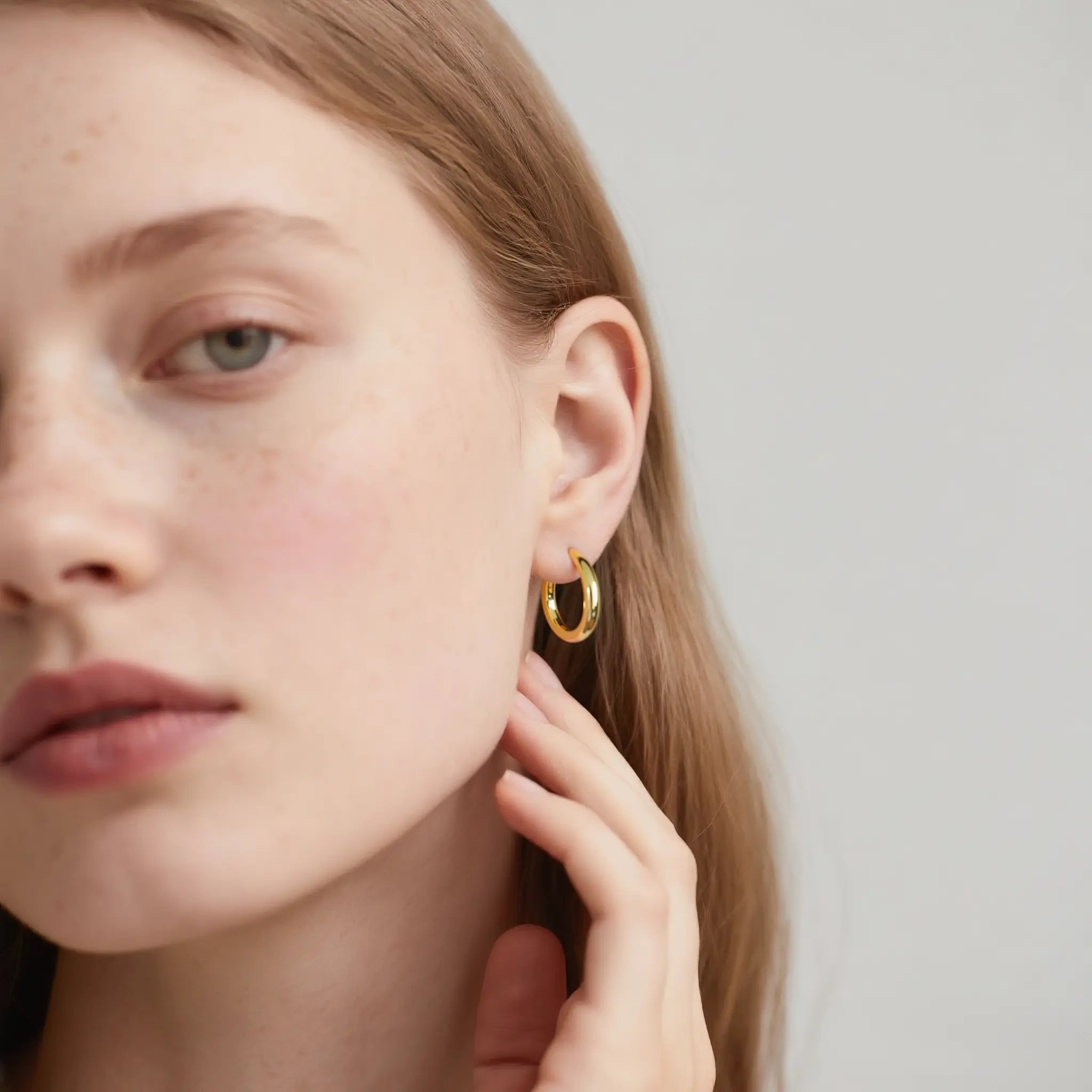 Close-up of a person wearing gold hoop earrings with a neutral background