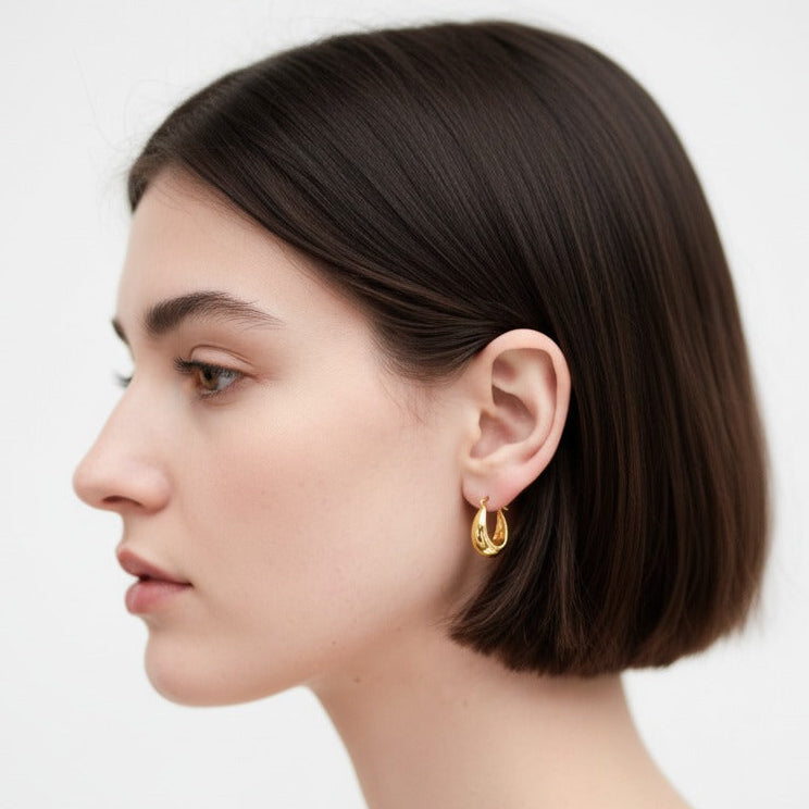 Woman wearing gold hoop earrings against a white background