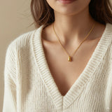 Close-up of a person wearing a gold necklace with a teardrop pendant against a neutral background.
