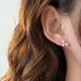 Model wearing delicate gold mini bow stud earrings with white enamel
