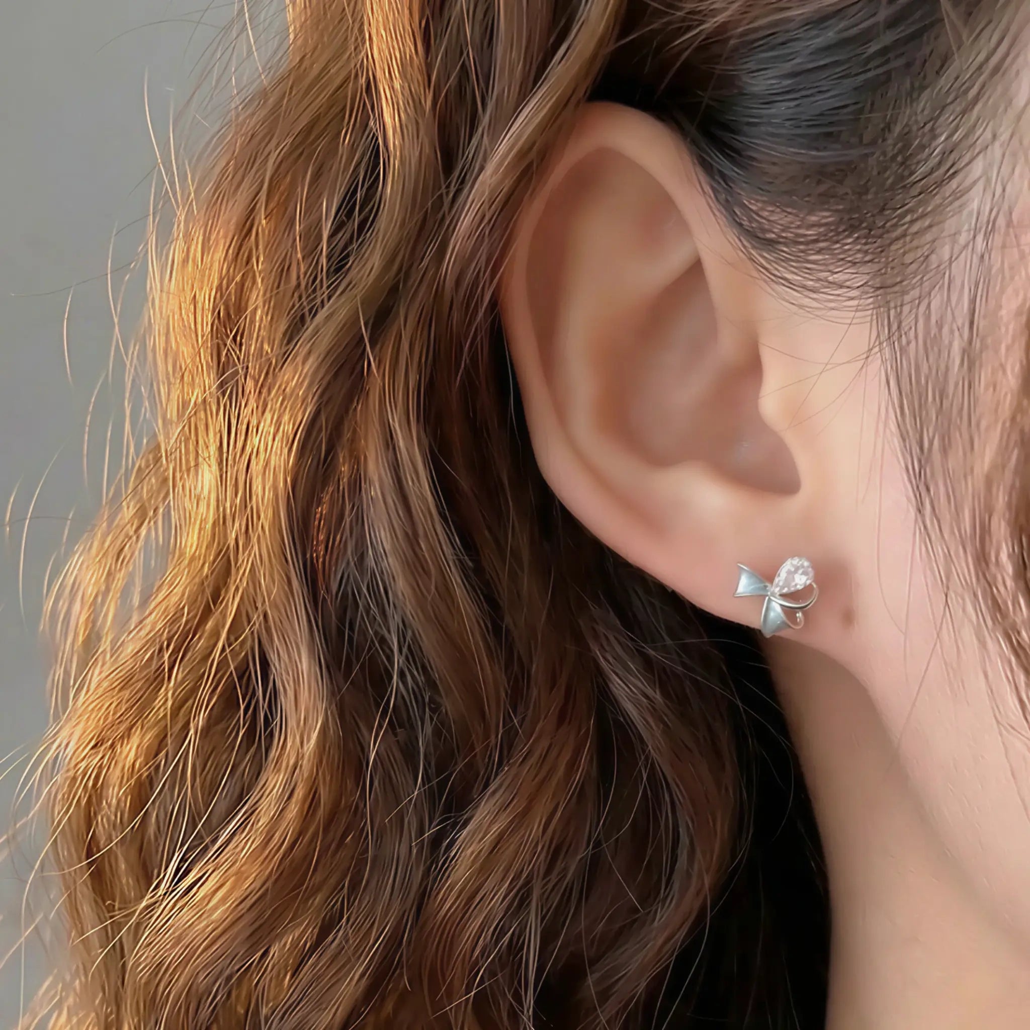 Model wearing delicate silver mini bow stud earrings with blue enamel