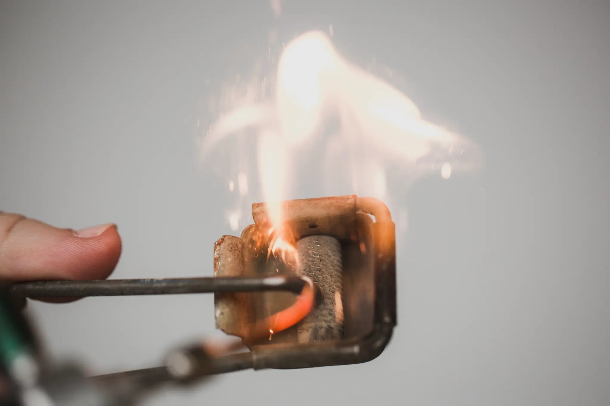 Flaming matchbox held by tongs against a gray background