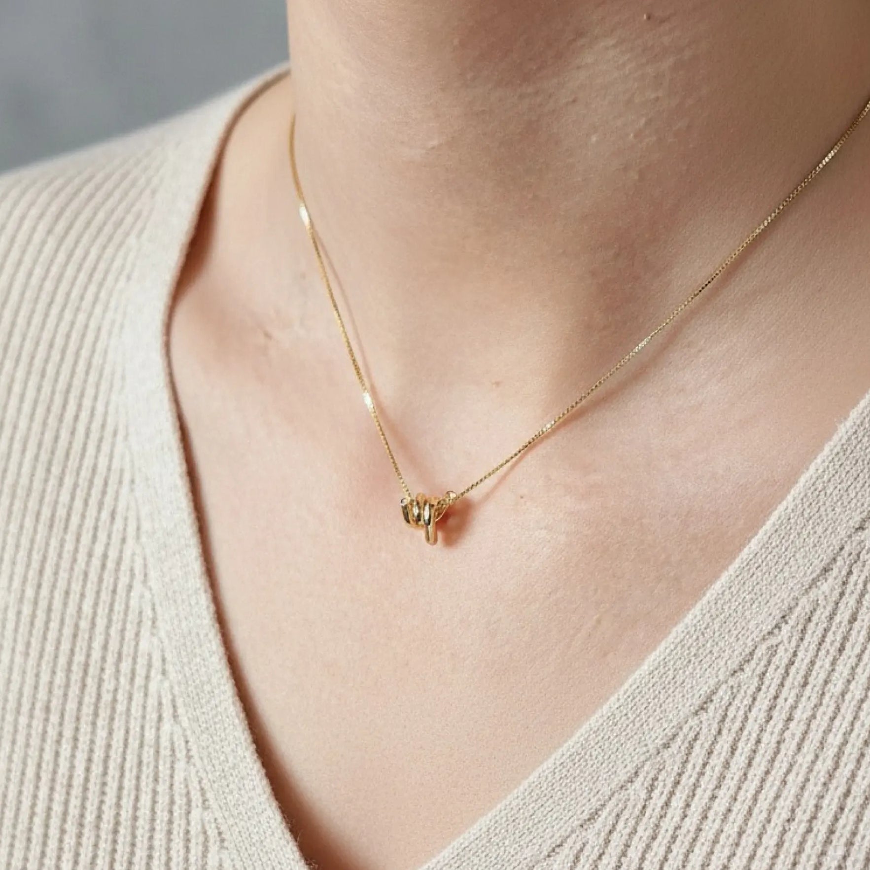 Gold necklace with a small pendant on a person wearing a beige sweater.