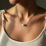 Close-up of a necklace with a pearl pendant worn by a person.