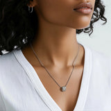 Woman wearing a silver necklace with a pendant against a neutral background