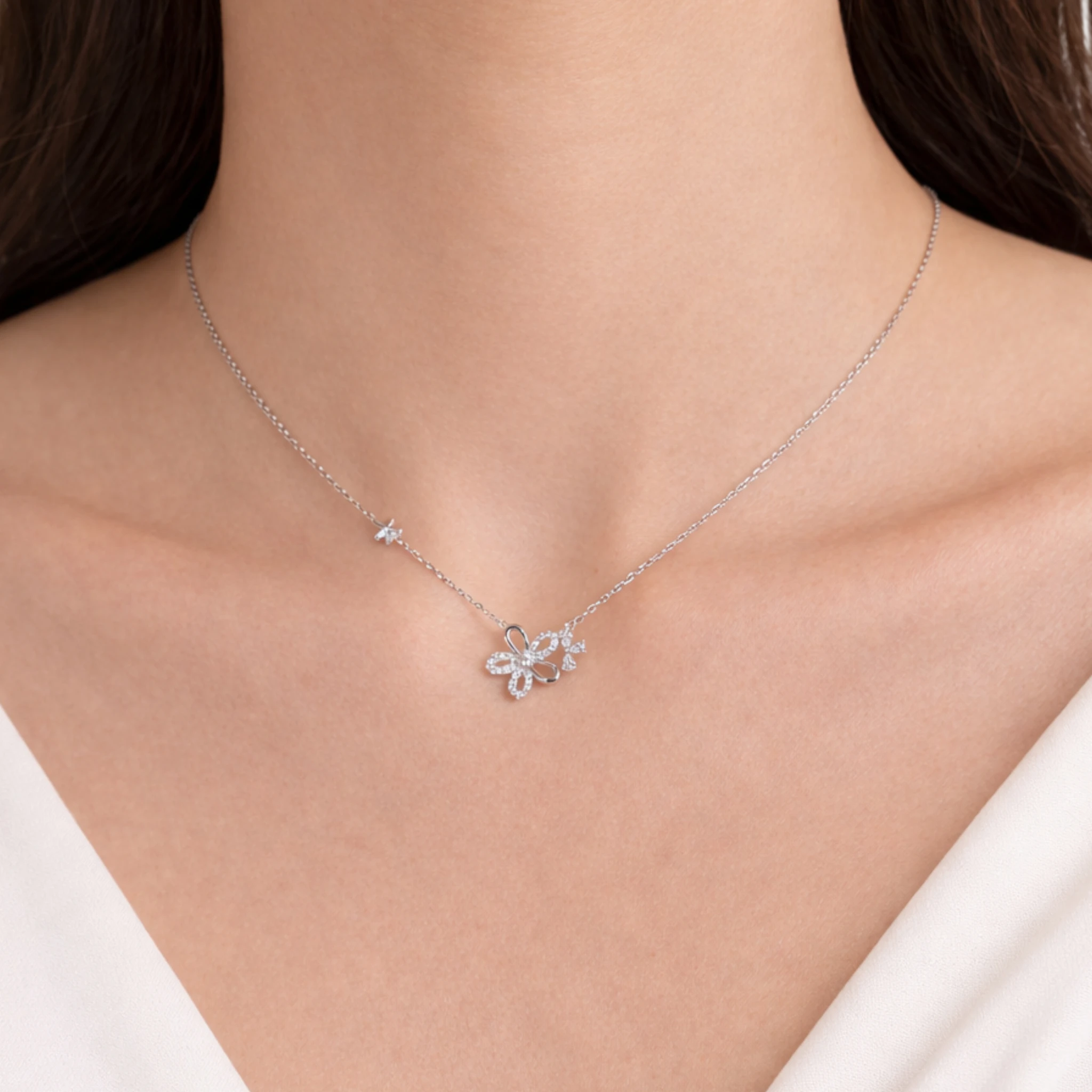 Silver necklace with a floral pendant on a person wearing a white top.
