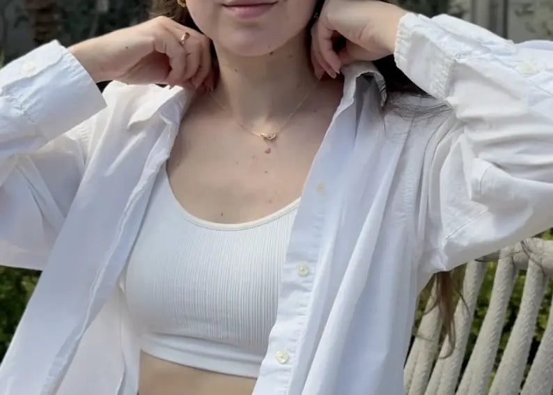 Woman wearing a white shirt over a white crop top and denim shorts, sitting outdoors showcasing effortless and everyday style jewelry