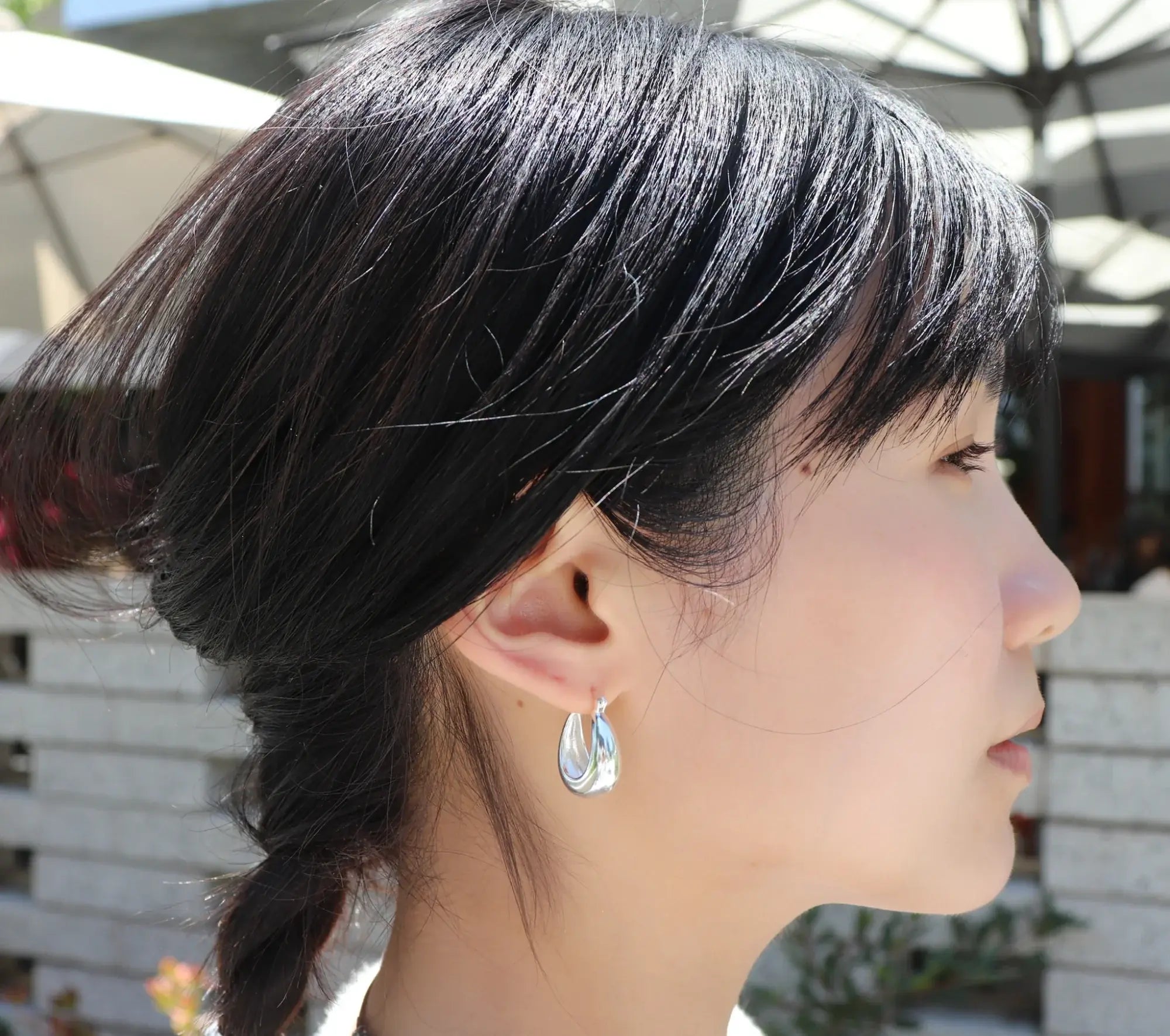Close-up of a person wearing silver hoop earrings that is premium, shine and classic 